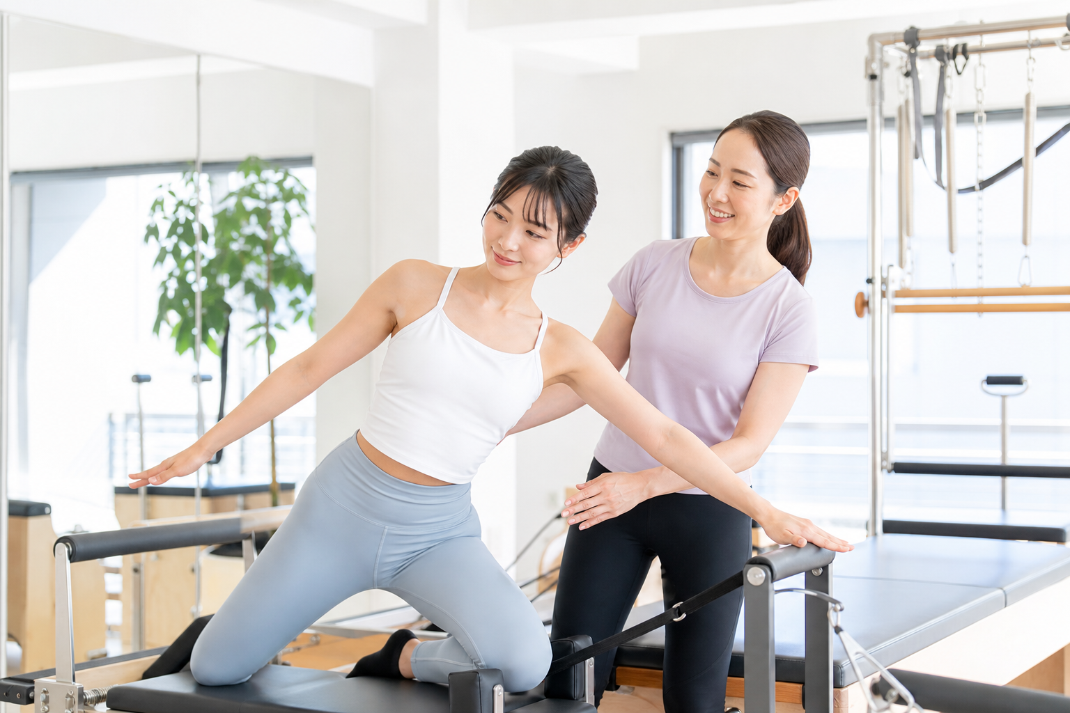 明るいスタジオでピラティスマシン(リフォーマー)を使い、インストラクターの指導を受けながら正しいフォームでエクササイズを楽しんでいる女性の様子。姿勢が美しく、健康的で前向きな雰囲気、スタジオ内は白を基